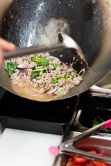 Chef cooking stir-fried vegetables and beef in a wok on a professional kitchen stove. Top-down view of Thai or Asian cuisine in preparation.