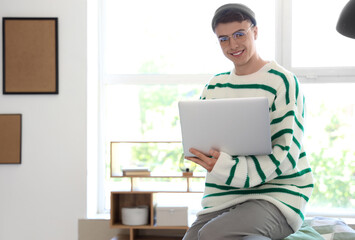 Young man in eyeglasses using laptop at home