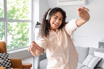 Young African-American woman in headphones dancing at home