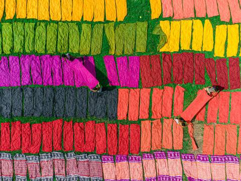Narayanganj, Bangladesh - 01 October 2023: Aerial view of vibrant textiles spread across the green field, creating a kaleidoscope of colors under the sun.
