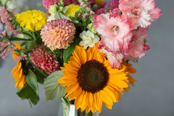 Vibrant bouquet of sunflower, dahlias, and gladiolus in vase against gray background