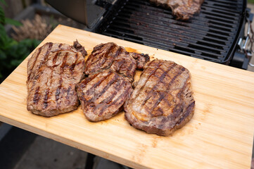 Grilled ribeye steaks on wooden board near outdoor grill