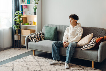 Young man sitting on sofa looking pensive in modern living room