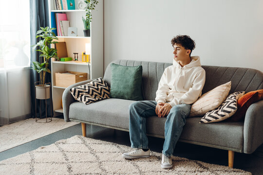 Young man sitting on sofa looking pensive in modern living room - Powered by Adobe