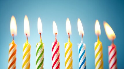 Ten colorful birthday candles with bright flames stand aligned horizontally against a blue background,