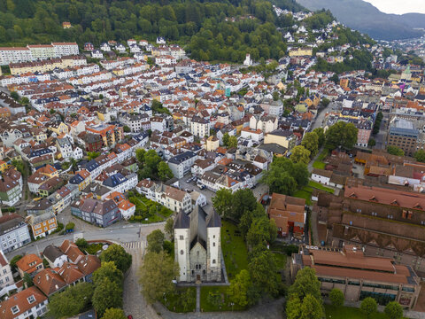 Aerial view of St. John's Church standing prominently amid a sea of red-roofed buildings and lush green trees nestled at the foot of Mount Fl&Atilde;&cedil;yen, Bergen, Vestland, Norway.