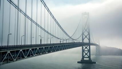 Obraz premium Foggy suspension bridge disappearing into thick mist over calm water at early morning — mysterious and minimal urban scene ideal for travel, engineering, design and atmospheric visuals