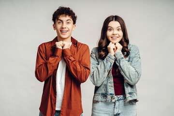 Surprised teenagers holding hands together under chin looking excited and amazed by unexpected...