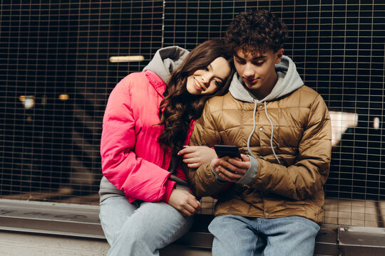 Young couple using smartphone and smiling while sitting next to a metal grid