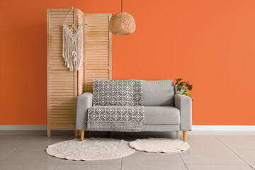 Comfortable sofa and folding screen near orange wall in interior of living room