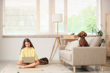 Sporty teenage girl with Poodle dog using laptop at home