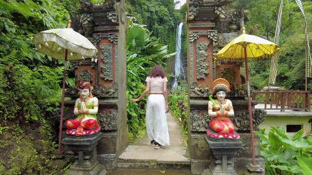 Young woman in a flowing white skirt walking towards Gitgit waterfall in Singaraja ,Bali