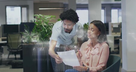 Leaning coworkers wearing professional attire studying printed document on armchair in open office