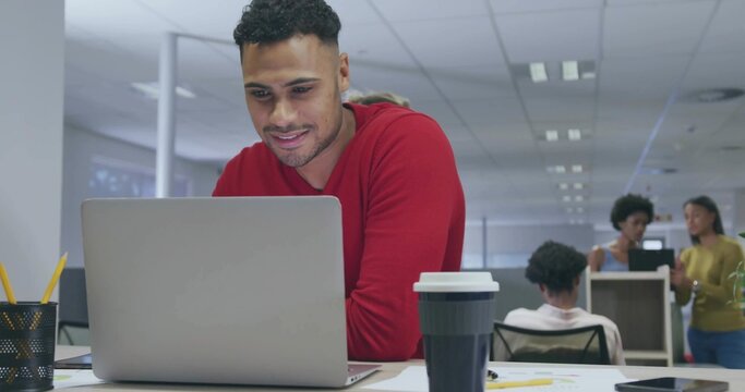 Working man in red sweater typing on silver laptop at open-plan office, with mug pencils smartphone - Powered by Adobe
