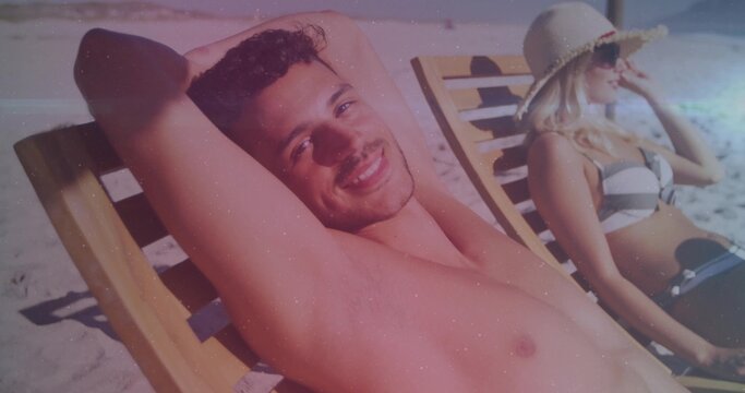 Couple reclining on beach loungers at sand dunes, wearing swimwear and straw sun hat - Powered by Adobe
