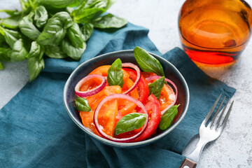 Bowl of fresh tomato salad with red onion and basil leaves on grey background, closeup