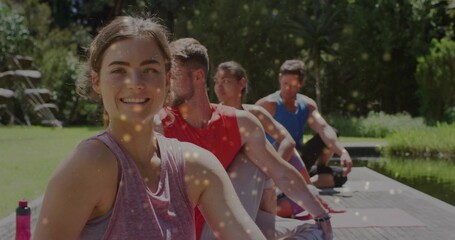 Sitting woman in pink tank and grey leggings twisting by pond with yoga mats, copy space