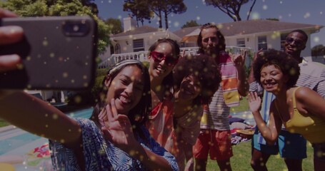Group of six friends taking selfie on lawn beside backyard pool, with smartphone and umbrella