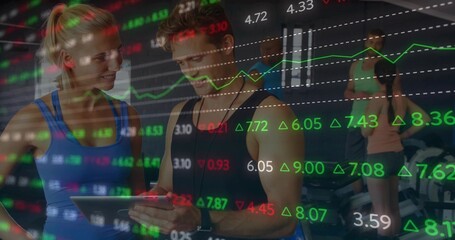 Examining tablet tracking performance trainer and client in gym studio, market charts overlay