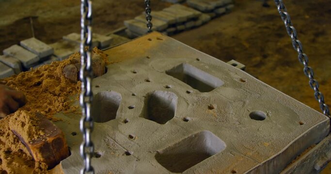 Packing worker hand molding sand around sand casting mold board in workshop, with lifting chains
