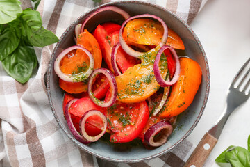 Bowl of fresh tomato salad with red onion and basil leaves on white background