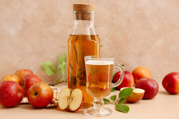 Bottle and glass cup of fresh apple cider with fruits on beige background