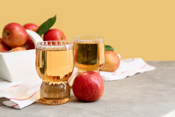 Glasses of fresh apple cider and basket with fruits on grey table