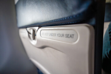 Close-up of a safety instruction sign on an airplane seat reading Life vest under your seat. In-flight details, transportation safety, and air travel routine.