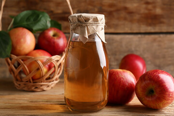 Bottle of fresh apple cider and wicker basket with fruits on wooden background