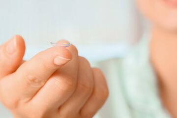 Naklejka premium Young woman holding contact lens on finger at home, closeup