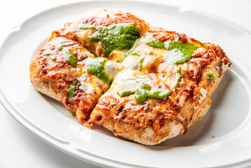 Rectangular pizza with thick rustic crust, melted cheese, tomato sauce, and green pesto, served on a white plate. Top-down view, gourmet style, vibrant colors