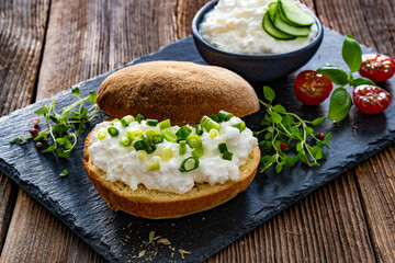 Cottage cheese roll with fresh herbs on stone board on wooden table