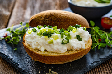 Cottage cheese roll with fresh herbs on stone board on wooden table