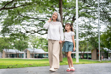 Fototapeta premium Old woman grandmother holding hand and walking with a kid girl granddaughter in the park or garden.