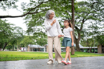 Fototapeta premium Old woman grandmother holding hand walking and talking to kid girl granddaughter in park or garden.