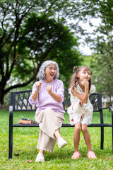 Fototapeta premium Old woman granny shaking arms cheering for a kid girl granddaughter dancing on grass in the park.