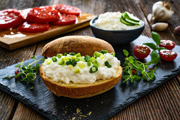 Cottage cheese roll with fresh herbs on stone board on wooden table