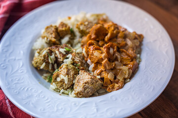 Plate of rice with meatballs and mushroom stew on wooden table surface