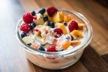 Bowl of fresh fruit salad with yogurt on wooden table surface from top view