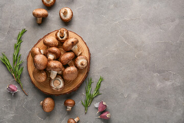 Wooden board  with fresh raw mushrooms, garlic and rosemary on grey background