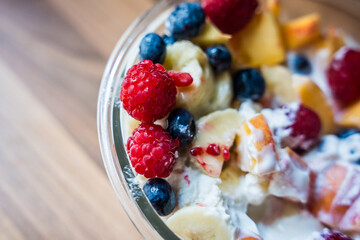 Fresh fruit salad with yogurt and berries in a glass bowl, close-up view