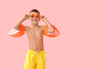 Cute little boy with inflatable armbands and sunglasses on pink background