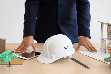 Male architect with hardhat, building model and tablet computer on table in office