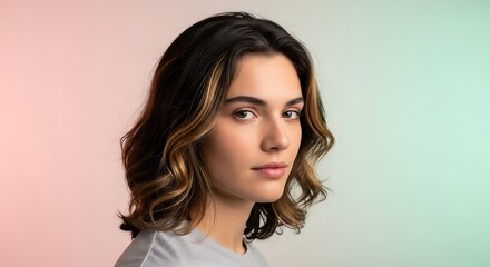 A young woman with wavy brown hair and highlights looks thoughtfully to the side against a soft pink and green gradient background.