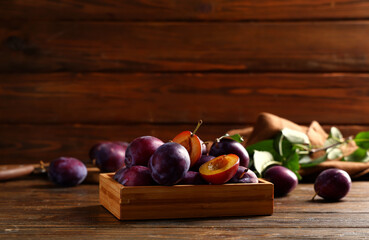 Box with fresh ripe plums on wooden background