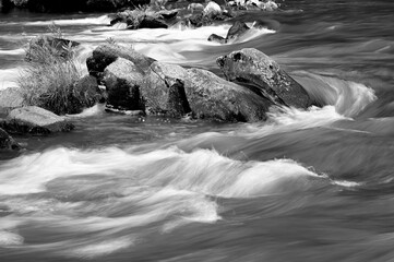 Black and white photo of whitewater rapids rushing around a group of rocks in the middle of a creek in Cherokee, North Carolina