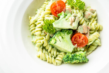 Vegetarian rotini pasta with creamy green sauce, broccoli, cherry tomatoes, and parsley. Fresh, healthy dish served on white plate. Top view, close-up, studio lighting
