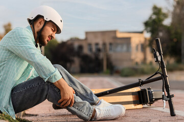 Young man fallen off his electric scooter sitting on bicycle path at city street © Pixel-Shot