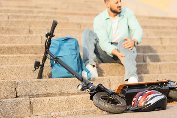 Obraz premium Young man fallen off his electric scooter sitting on stairs at city street