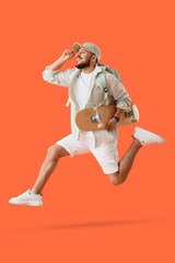 Handsome young man with skateboard jumping on orange background